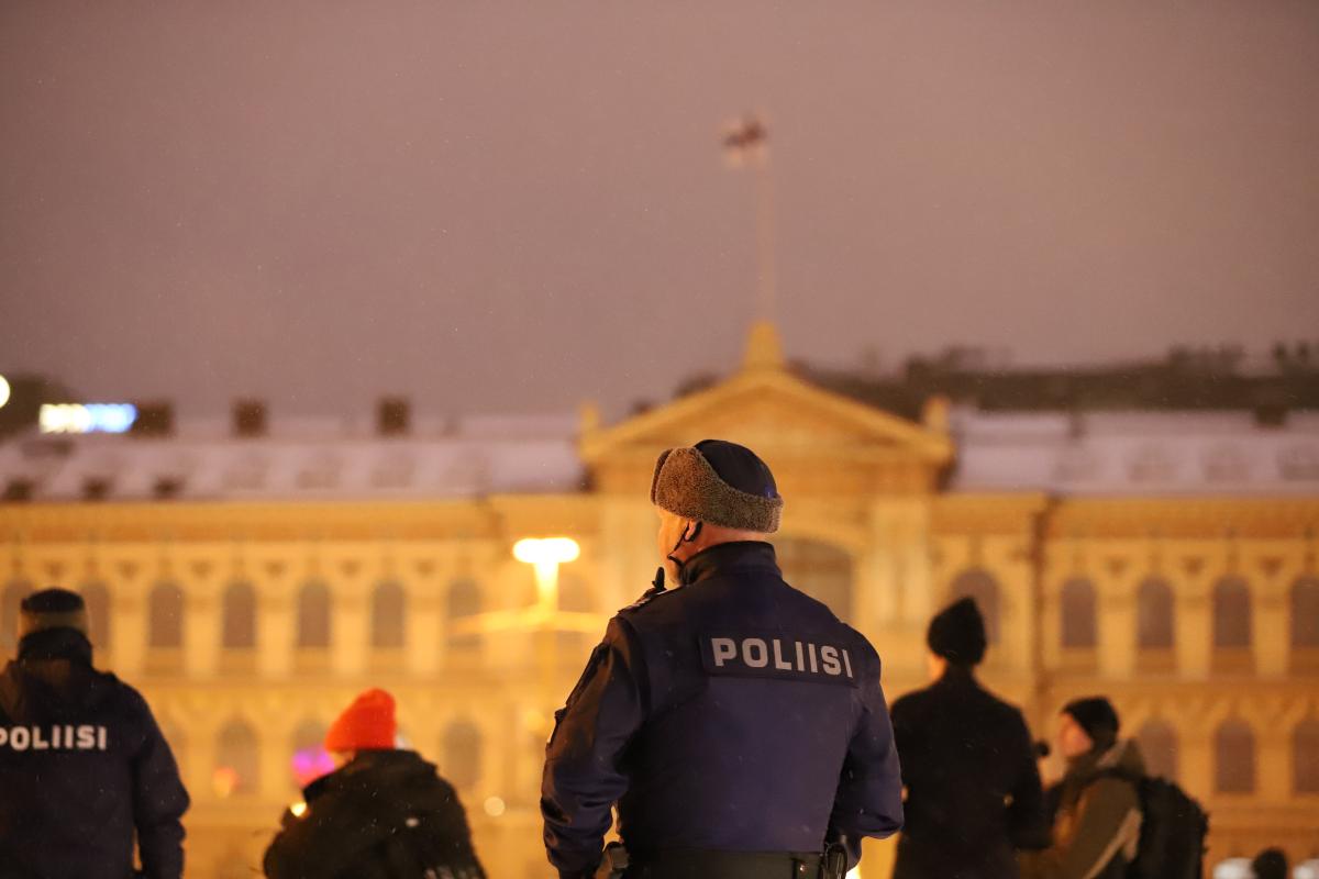 Poliisi seisoo rakennuksen edessä. Rakennuksen katolla liehuu Suomen lippu.