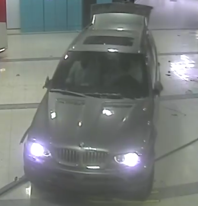 Harmaa BMW katumaasturi edestä sisällä kaksi ihmistä valkoissa paidoissa autossa takaluukku auki ja ajovalot päällä