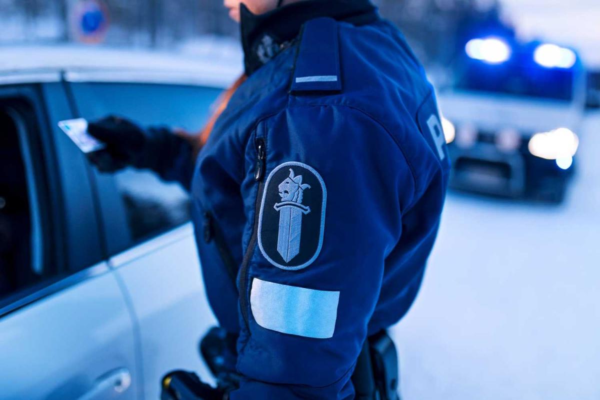 Poliisi tarkastaa ajokorttia liikennevalvonnassa, taustalla mustamaija lumisessa maisemassa.
