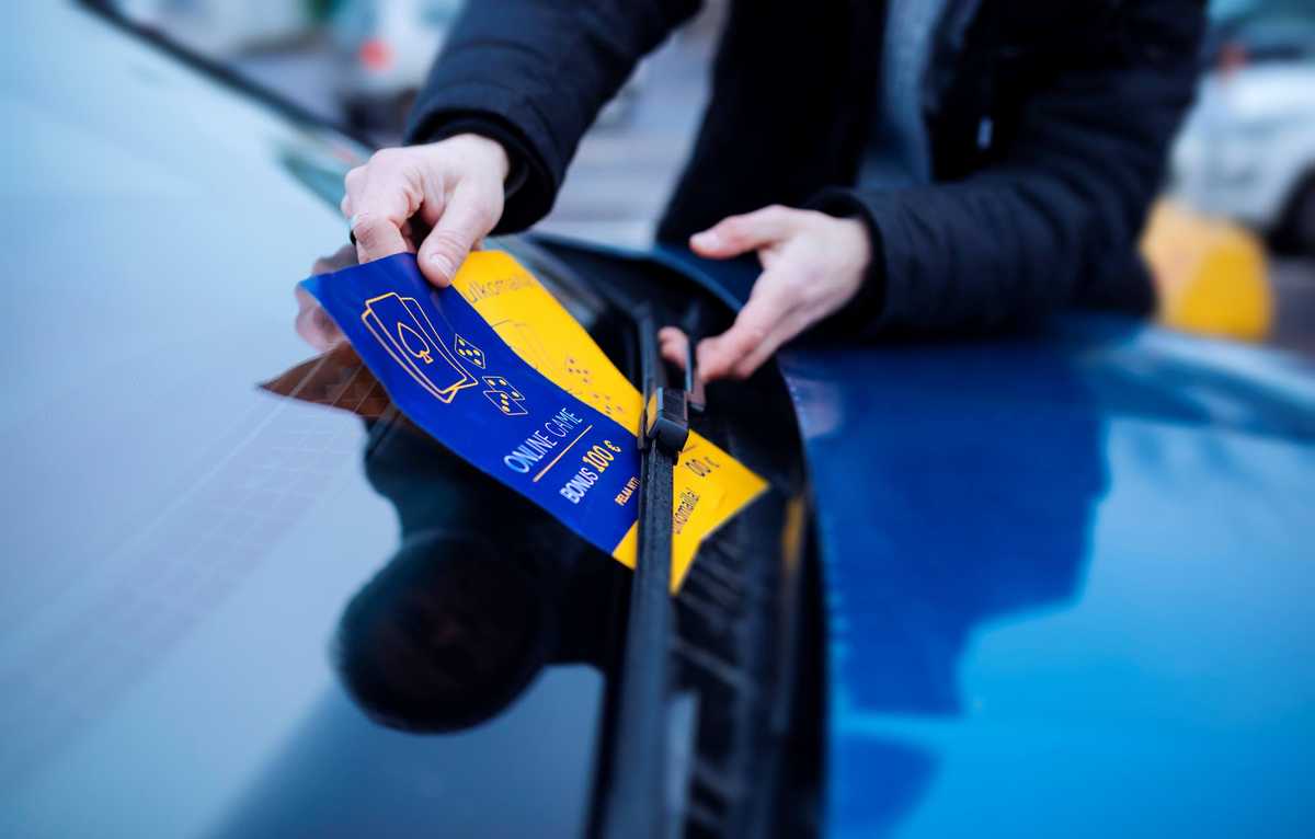 Marketing leaflets are being placed under windshield wipers of a parked car