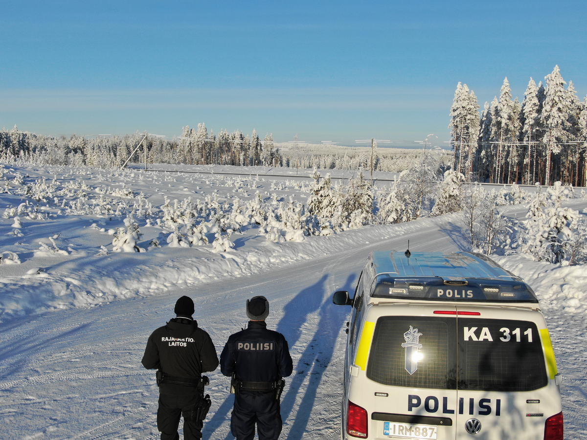 Rajavartija ja poliisi selin kameraan kuvattuna talvisessa maisemassa poliisiauton vieressä.