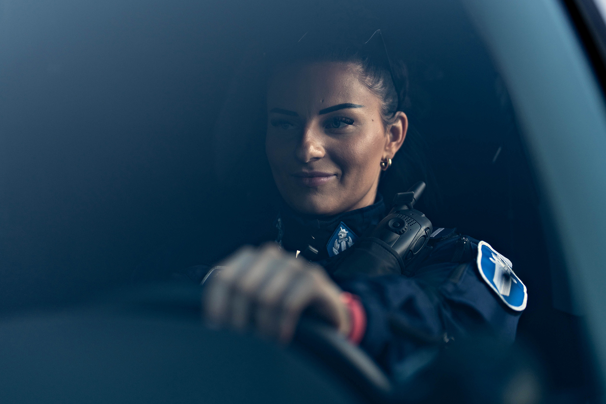 Poliisi istuu autossa ja katsoo vasemmalle, käsi ohjauspyörällä.