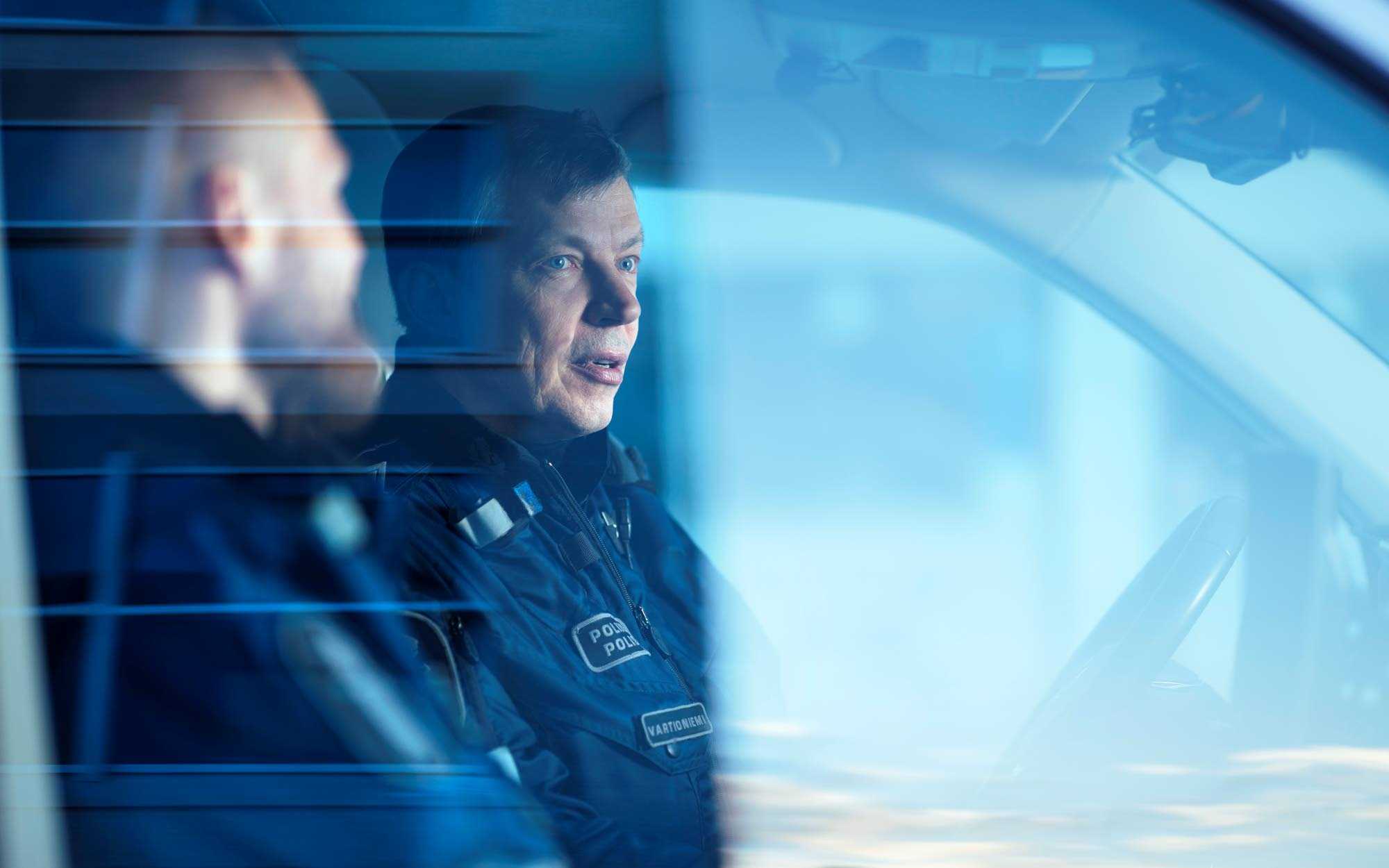 Police officers in a police car photographed through a window. 