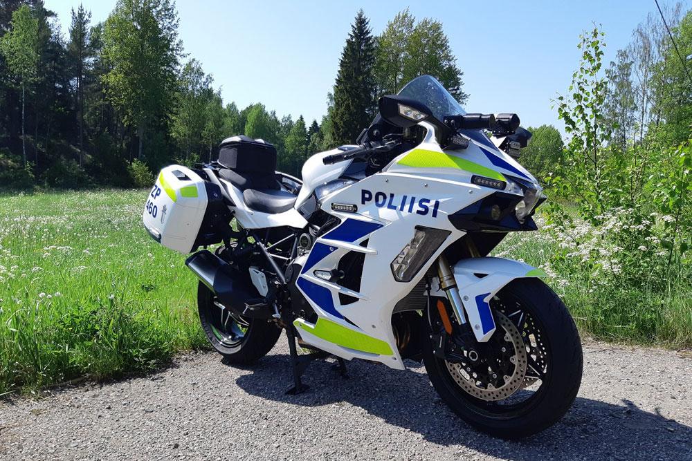 Police motorbike parked at the roadside, with a summery meadow in the background. 