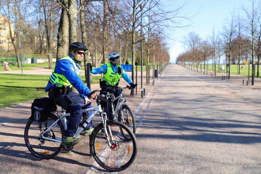 Kaksi polkupyöräpoliisia istuu pyörien satulassa ja katselee tyhjää Kaivopuistoa tien reunustolppiin nojaten. 