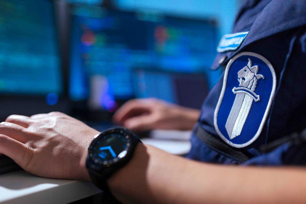A police officer’s hands on a keyboard with a watch and the police’s sword-and-lion emblem in the foreground.