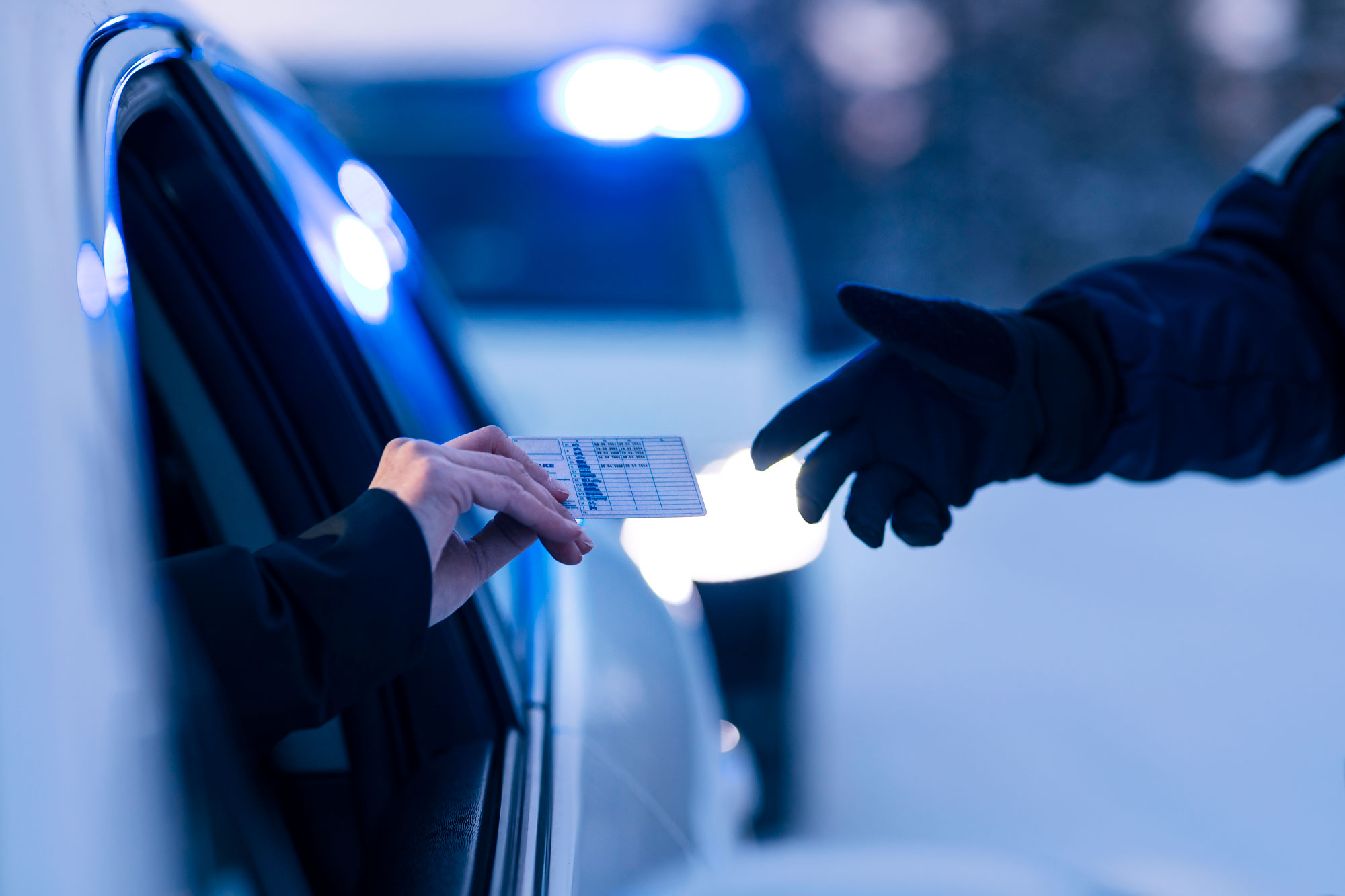 Asiakas ojentaa poliisille ajokortin henkilöauton ikkunasta. Ajokortti asiakkaan kädessä ja poliisin käsi ojentuneena ottamaan sitä. 