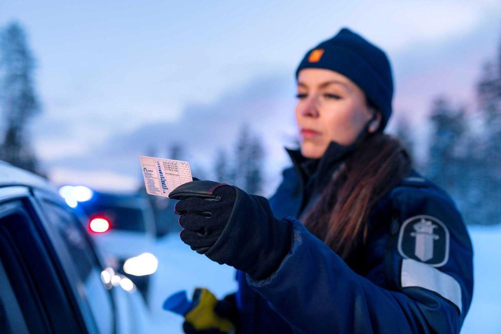 Poliisi tarkastelee pysäytetyn auton kuljettajan ajokorttia.