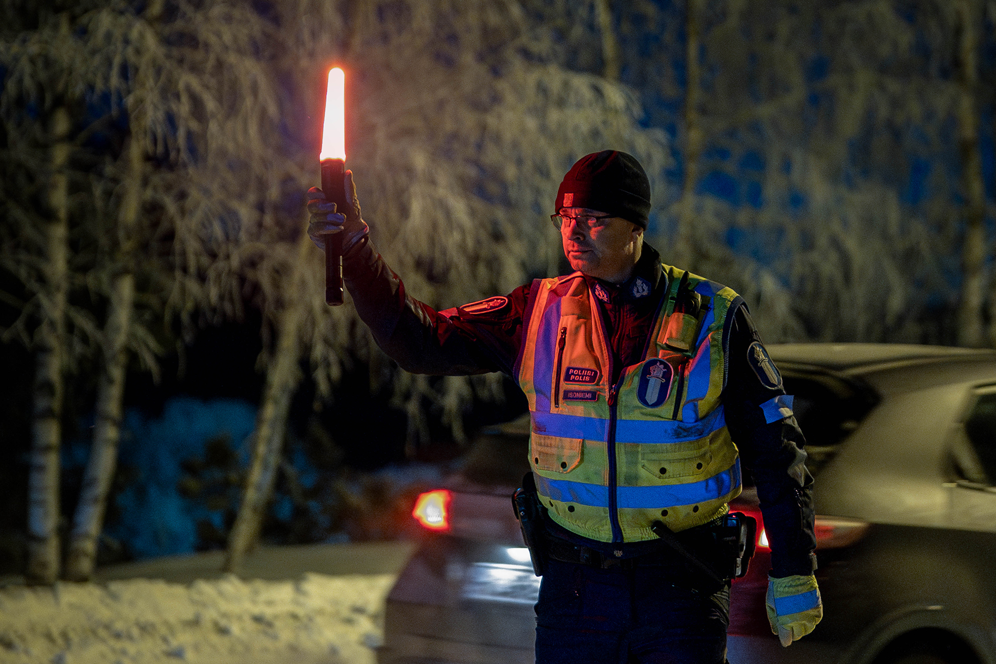 Huomioliiveihin pukeutunut poliisi pysäyttää autoilijan talvisessa ympäristössä ja näyttää pysäytysmerkkiä, jossa palaa punainen valo.