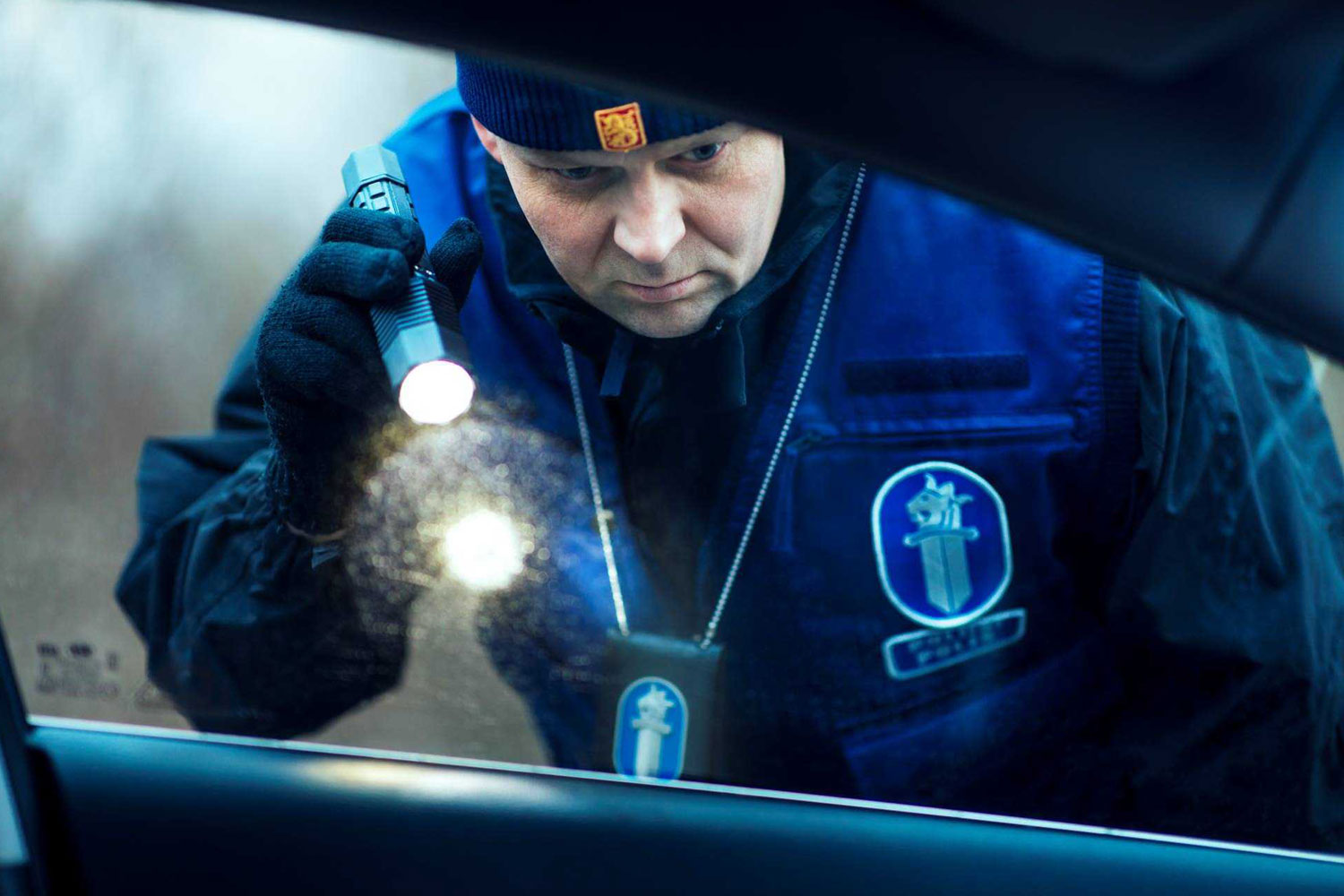 A police officer shining a torch into a car through a window. 