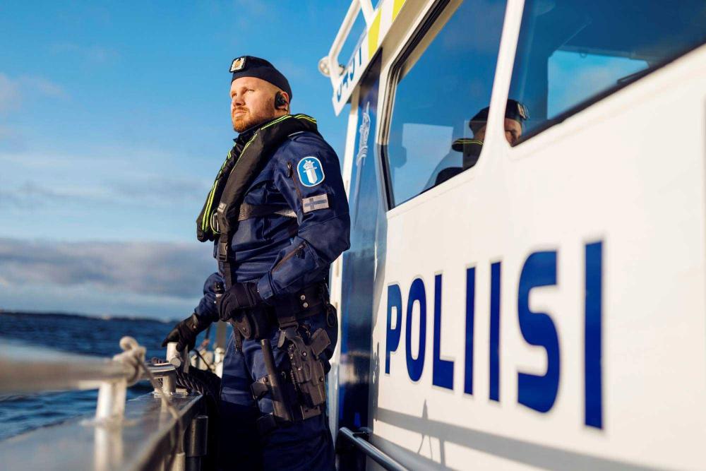 Venepoliisi seisoo poliisiveneen kannella kaiteeseen nojaten, vieressä näkyy poliisi-teksti veneen kyljessä.