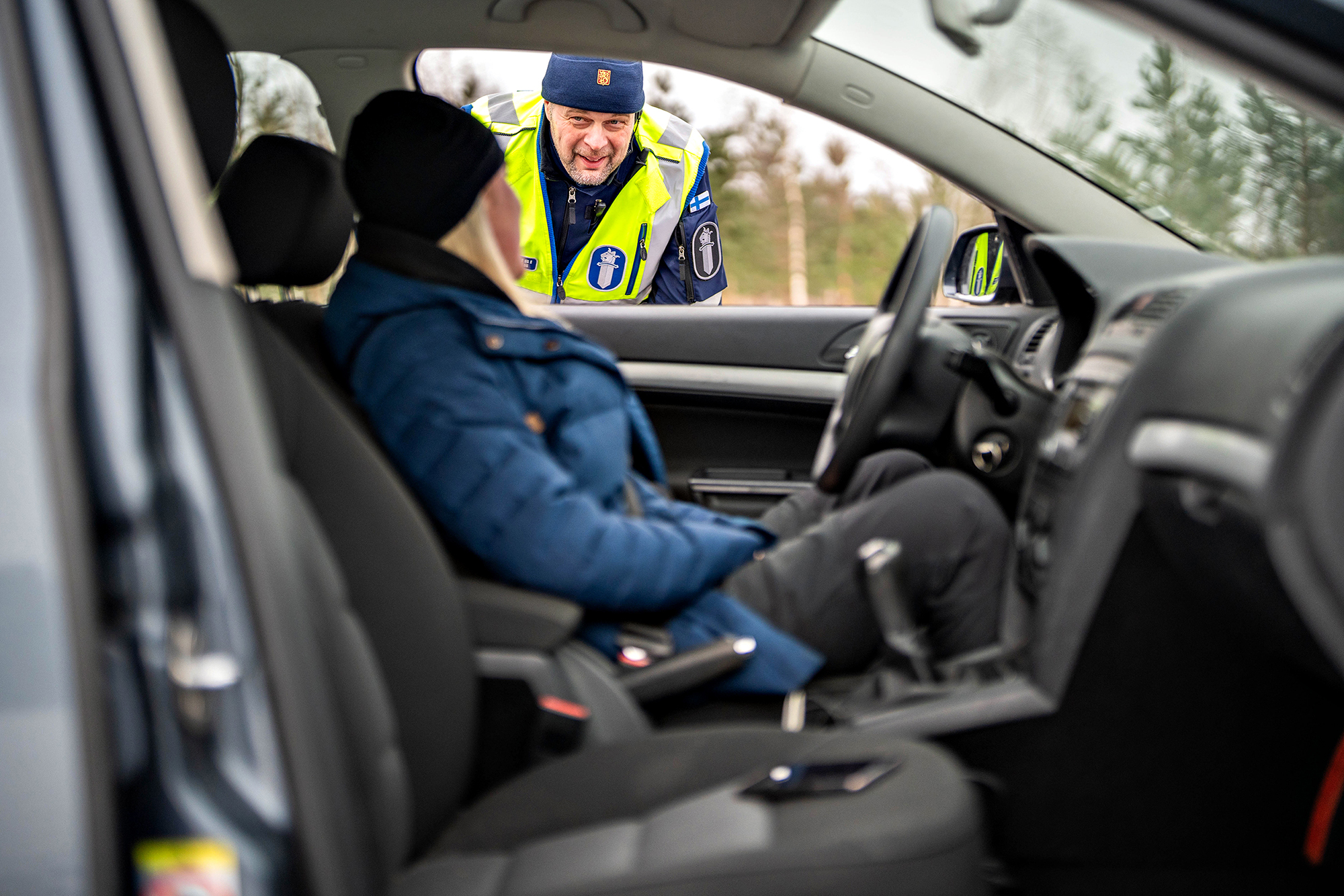 A police officer has stopped a car and is talking to the driver in winter conditions.
