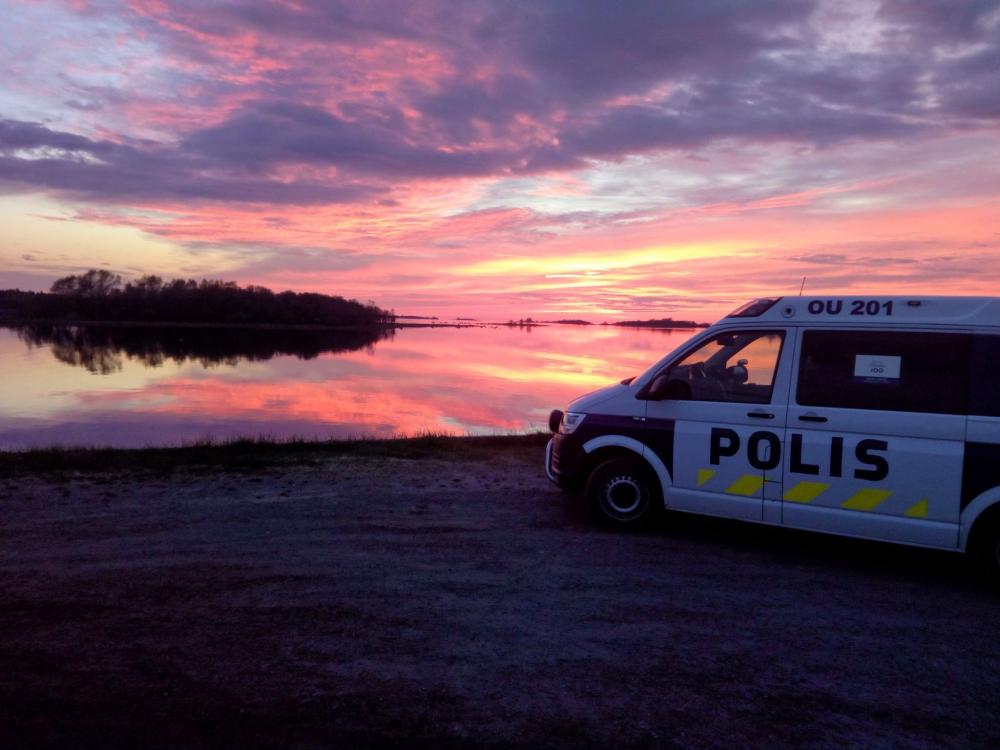  Police car on the beach. The sky glows red in the background.
