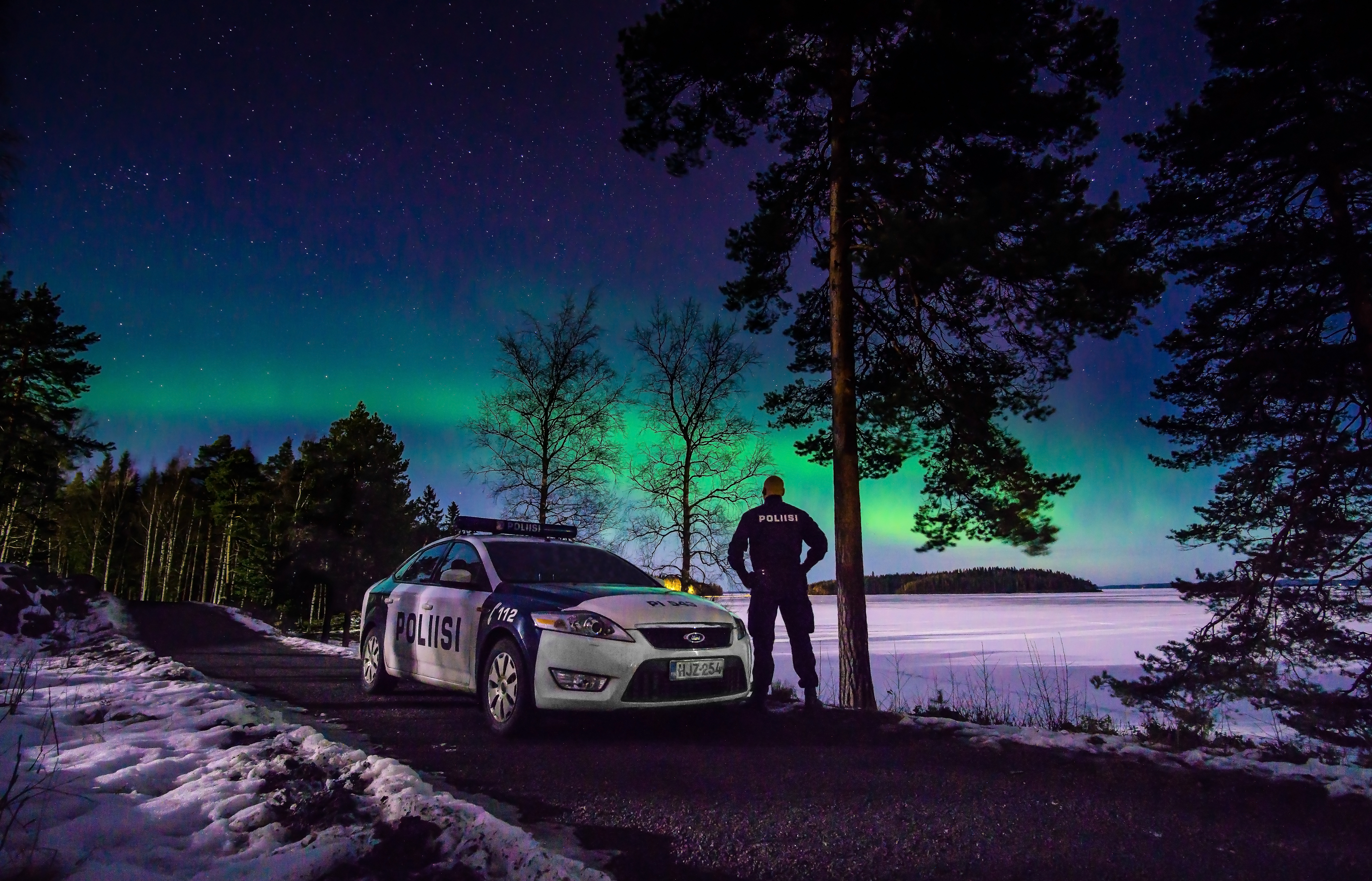 Police car and police on the lake in winter. Northern lights blazing in the background.