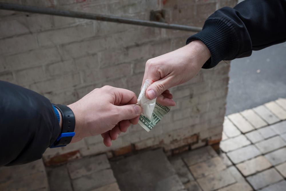 Drugs changing hands. The hands are holding a banknote and a bag of drugs. 