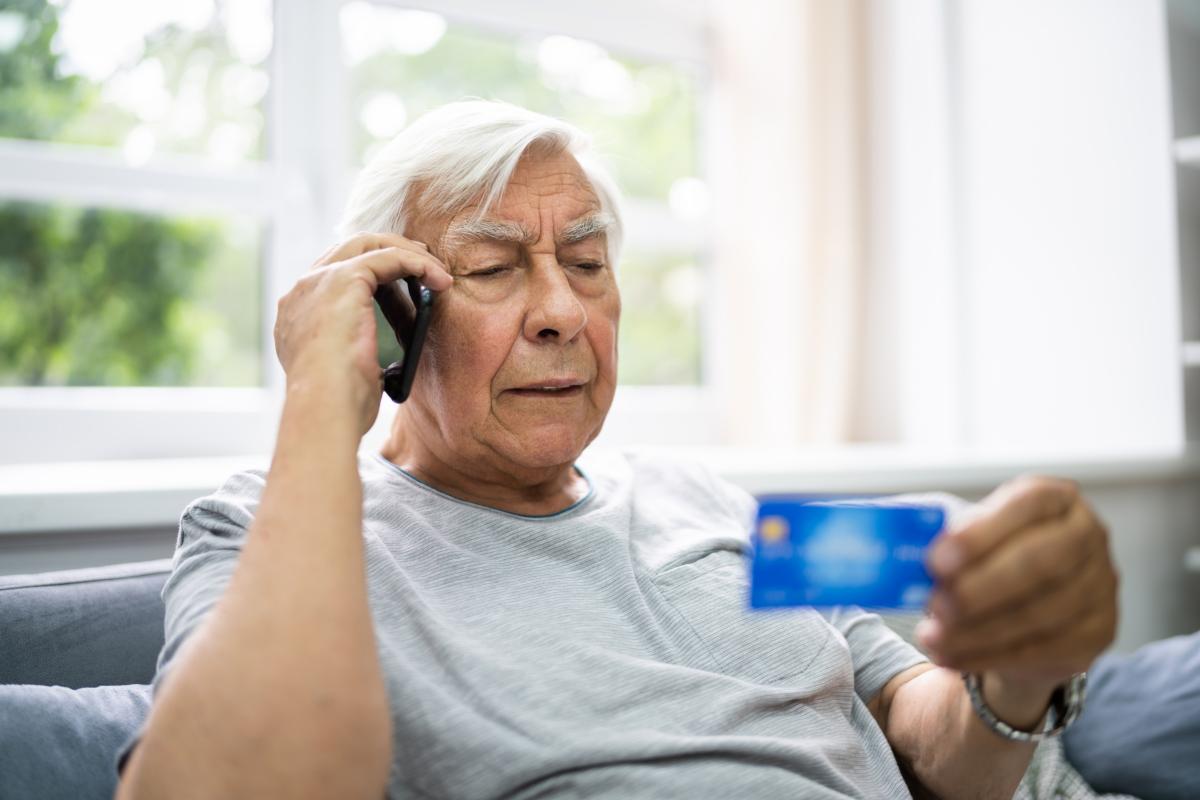 Vanhempi mies puhuu puhelimassa katsoen samalla kädessä olevaa pankkikorttia