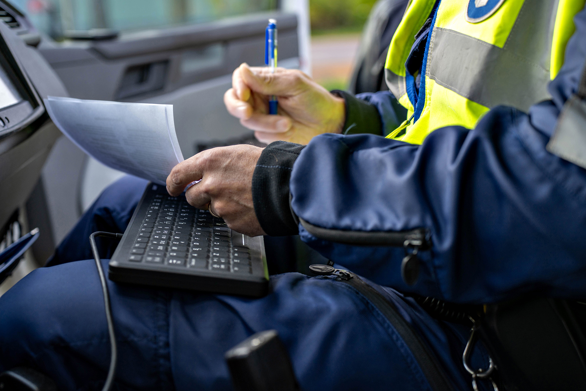 A police officer holds a traffic violation fine and presents it to the recipient. The officer’s hands, a computer keyboard and the document are visible. Illustrative image.