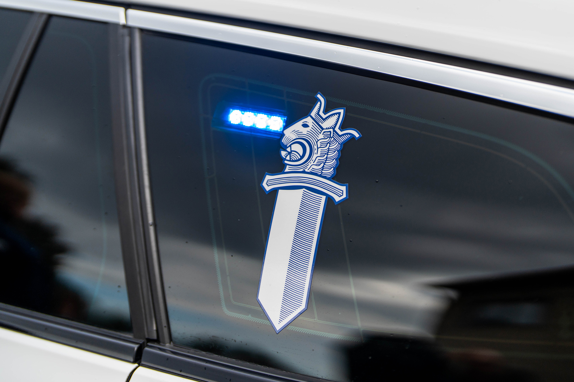 The lion emblem is visible on the side window of a police car and the blue emergency light is flashing.