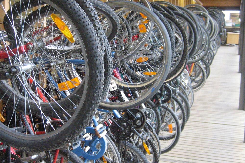 A line of bicycles in a bicycle parking rack against a wall. Tyres in the foreground. / Bicycles side by side in a police warehouse. Some in wall-mounted racks, some on the floor.