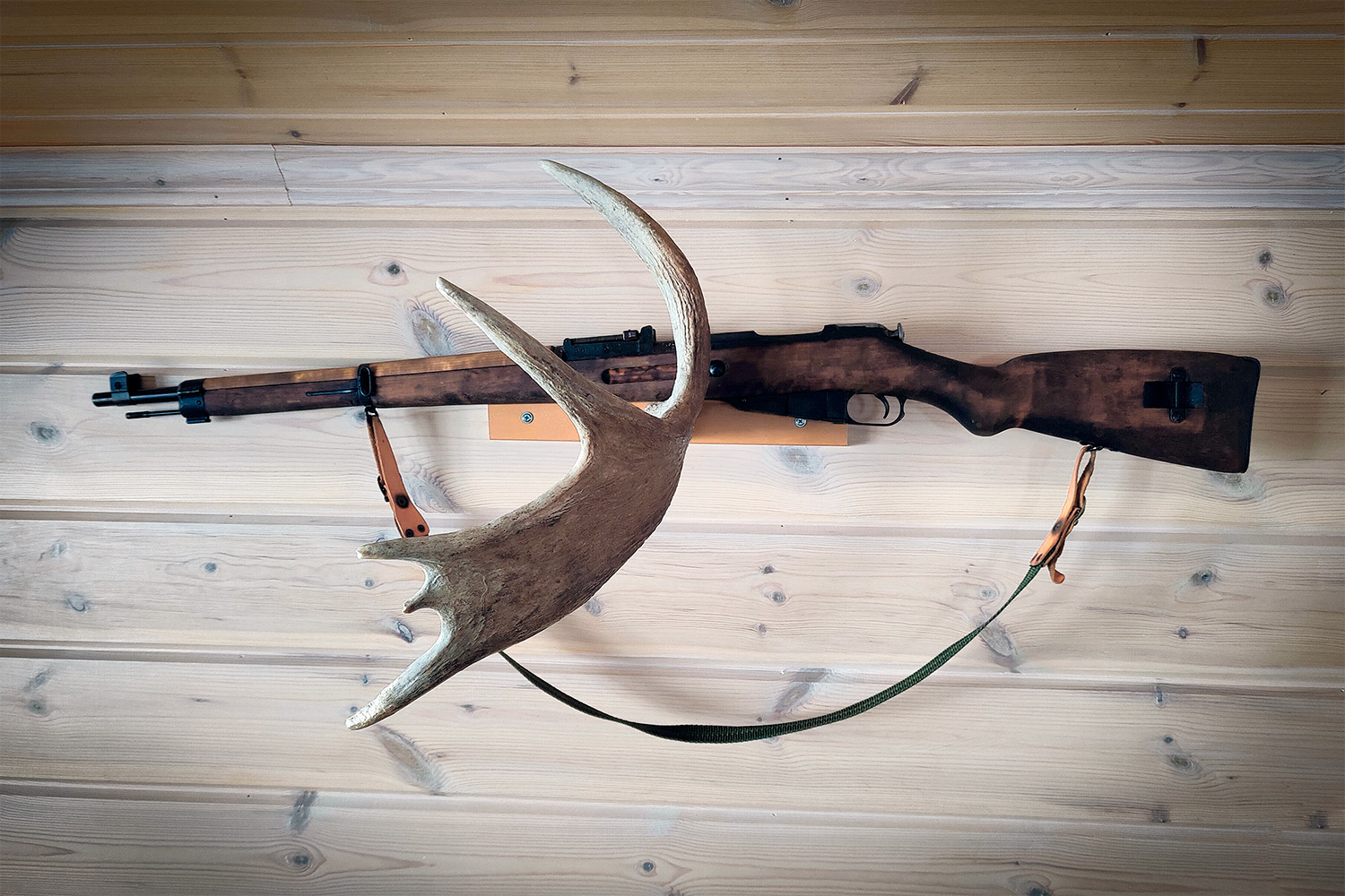 An old-style bolt-action rifle with a sling, suspended from a stand made of moose antler.