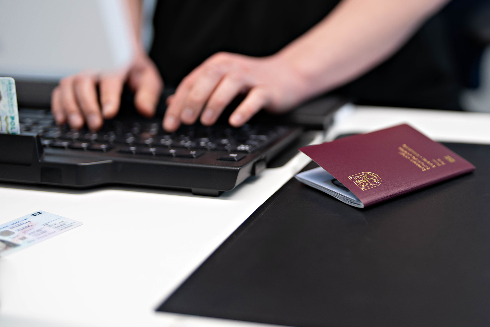 Tillståndssekreterarens händer skriver på ett tangentbord och ett pass ligger bredvid tangentbordet. Illustrationsbild.