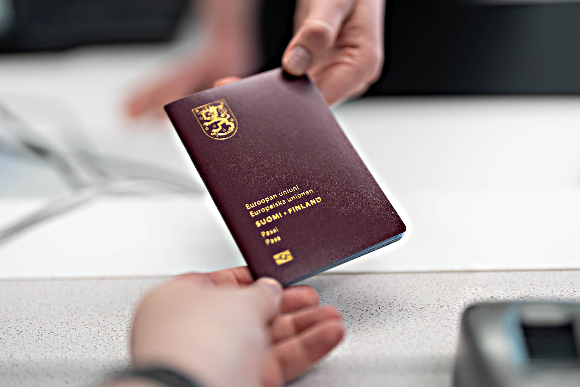 Lupasihteeri ojentaa passia asiakkaalle. Molempien kädet ja passi näkyvät.