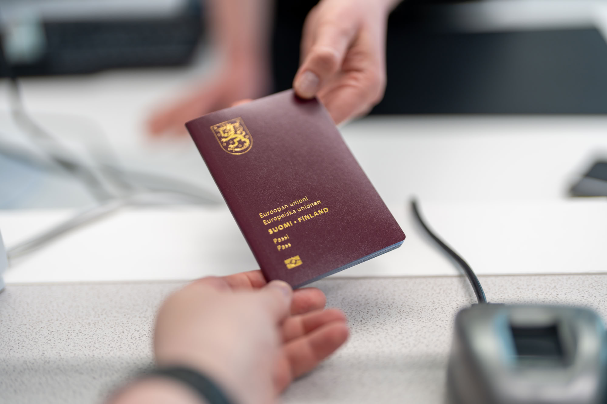 A permit clerk hands a passport to a customer. Both hands and the passport are visible.