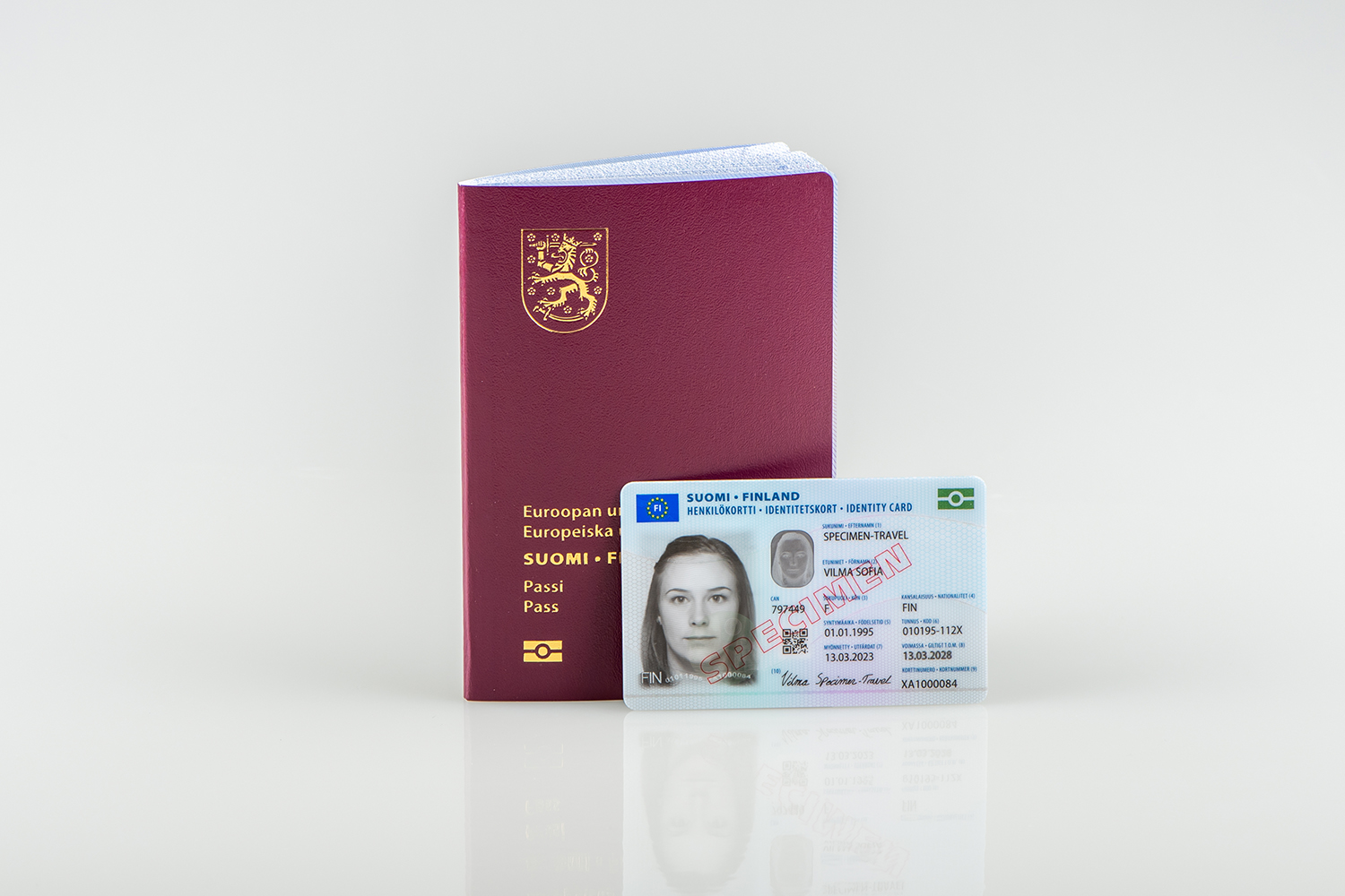 The burgundy cover of a standard Finnish passport. Finnish identity card with the text specimen in the foreground.