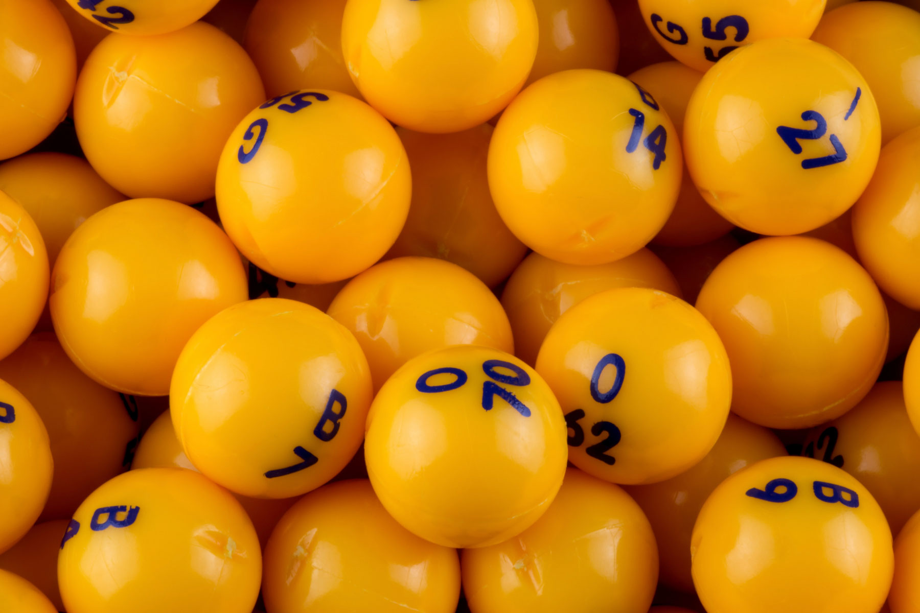 Yellow bingo balls from up close, in some of the balls, you can see a combination of a letter and a number. 
