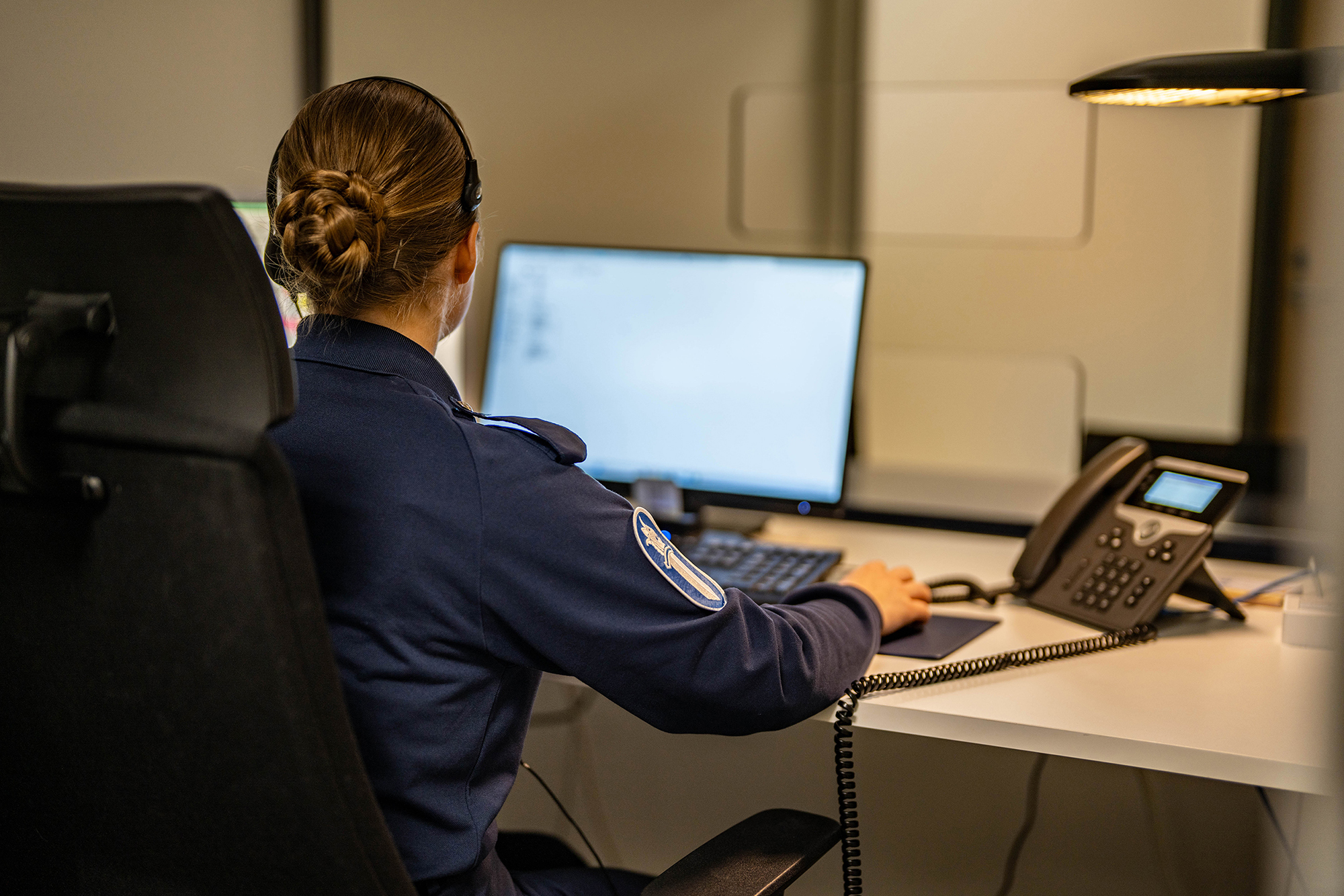 Poliisi työskentelee tietokoneella ja kirjaa rikosilmoitusta, taustalla asiakaspalvelutiski.
