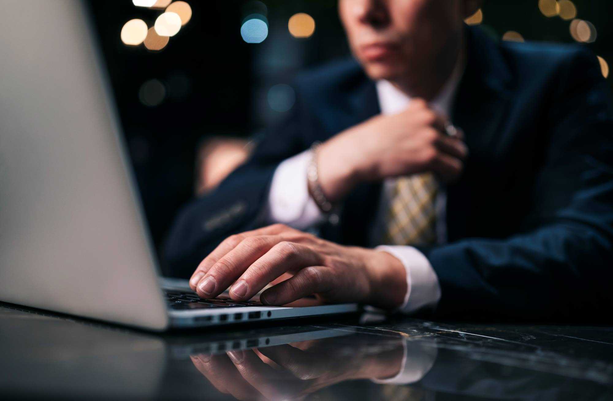 Pukuun ja solmioon pukeutunut mies katsoo kannettavaa tietokonetta.