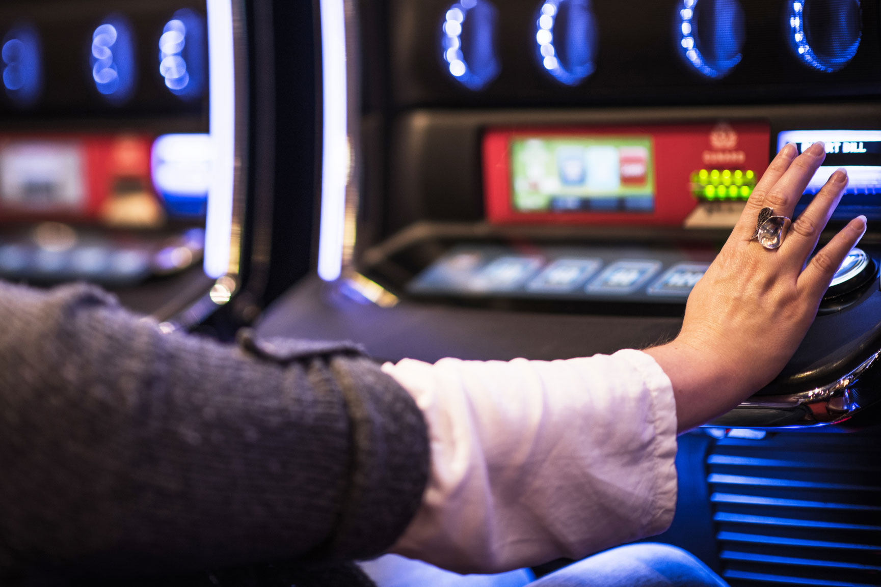 Ihminen pelaamassa raha-automaattia. Vain hänen kätensä näkyy raha-automaatin napilla.