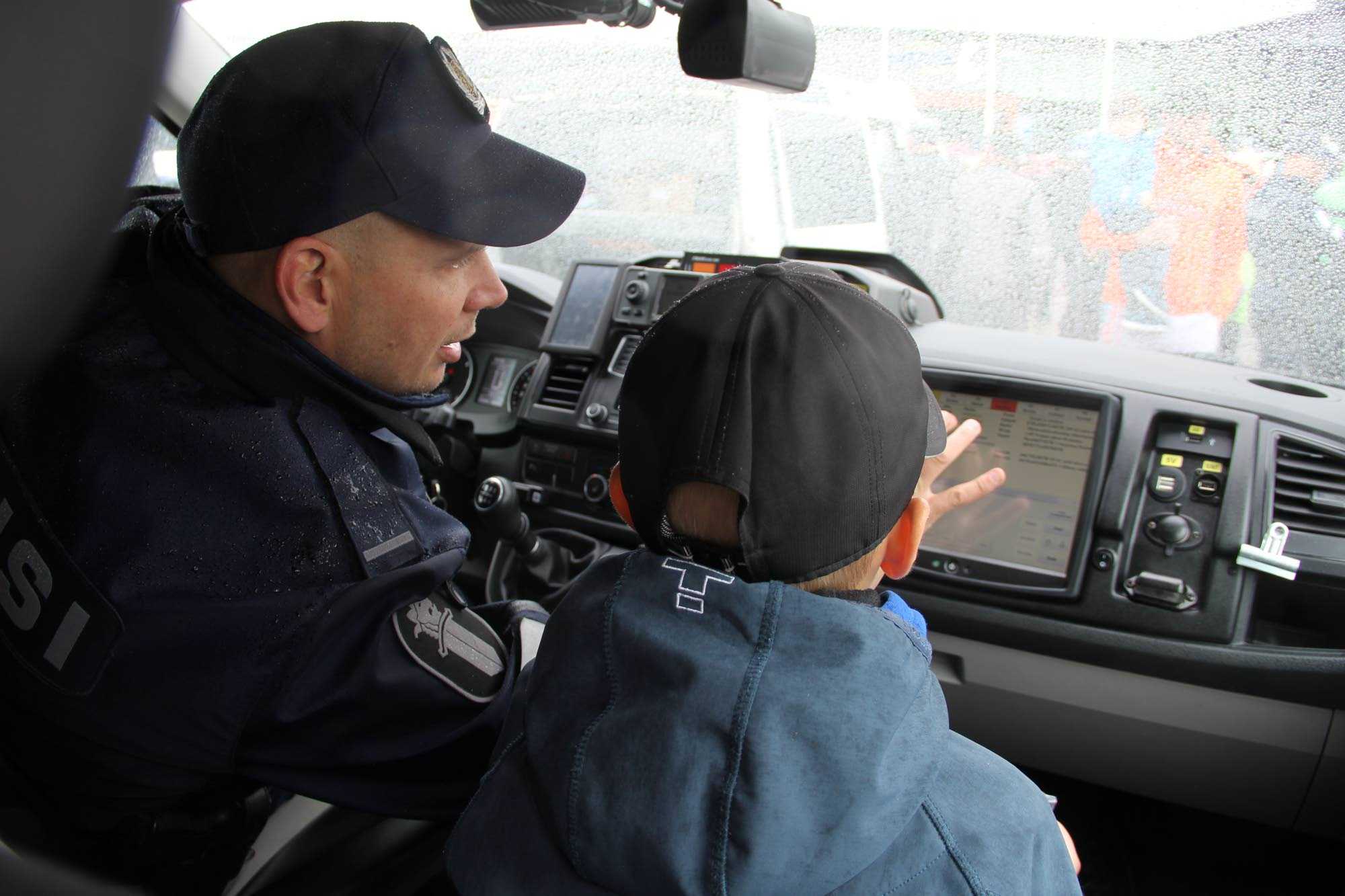 Poliisi esittelee lapselle poliisiauton laitteita.