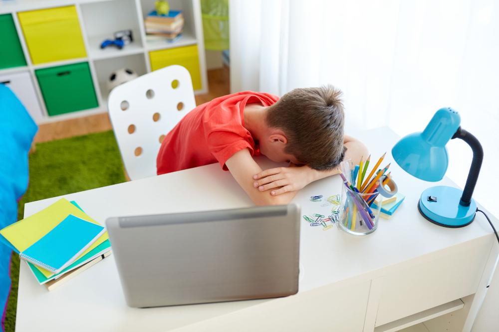 Ett barn lutar huvudet mot händerna vid en pulpet. På bordet en öppnad laptop. 