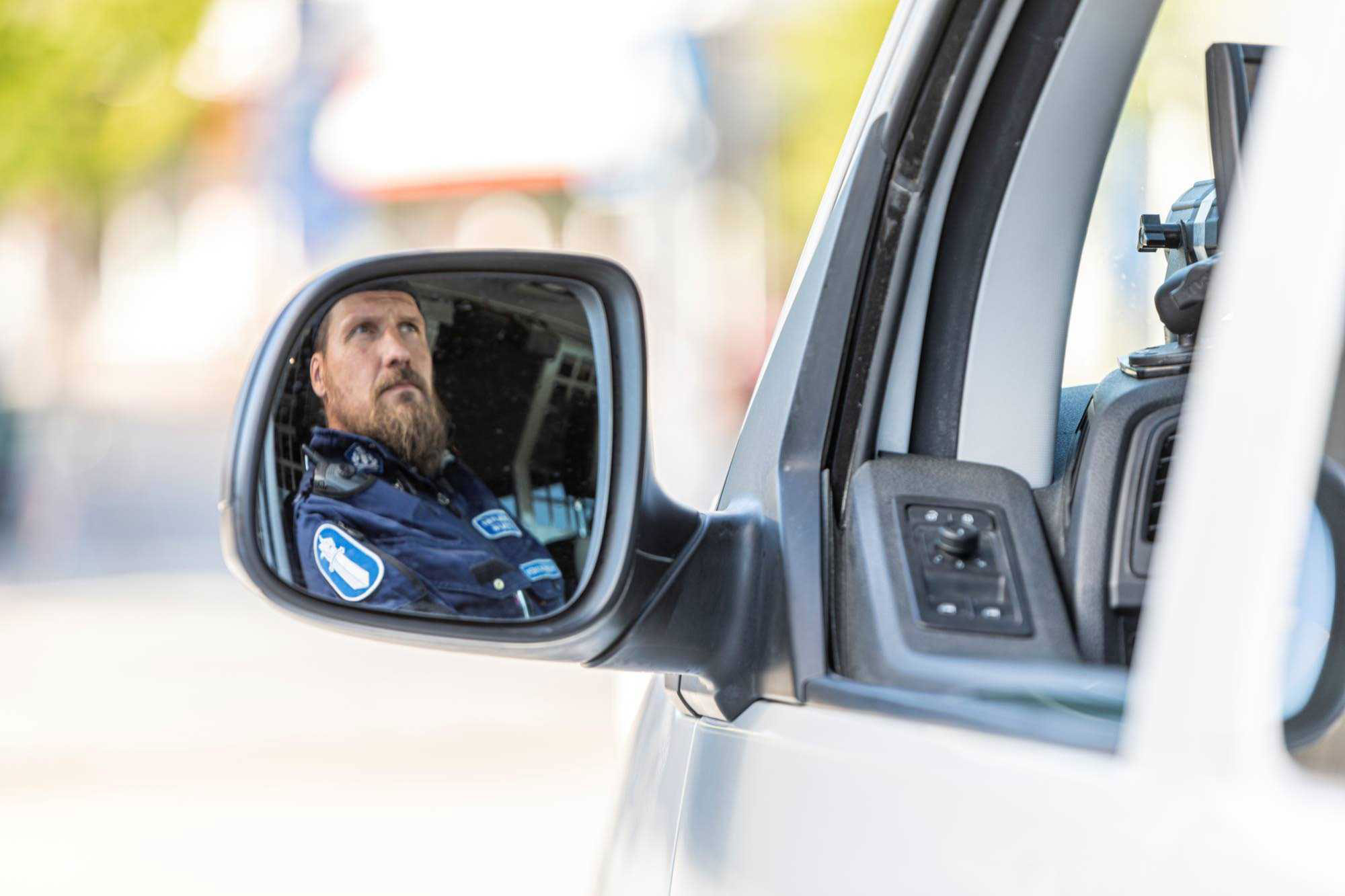 En konstapels ansikte skymtar i en polisbils sidospegel.