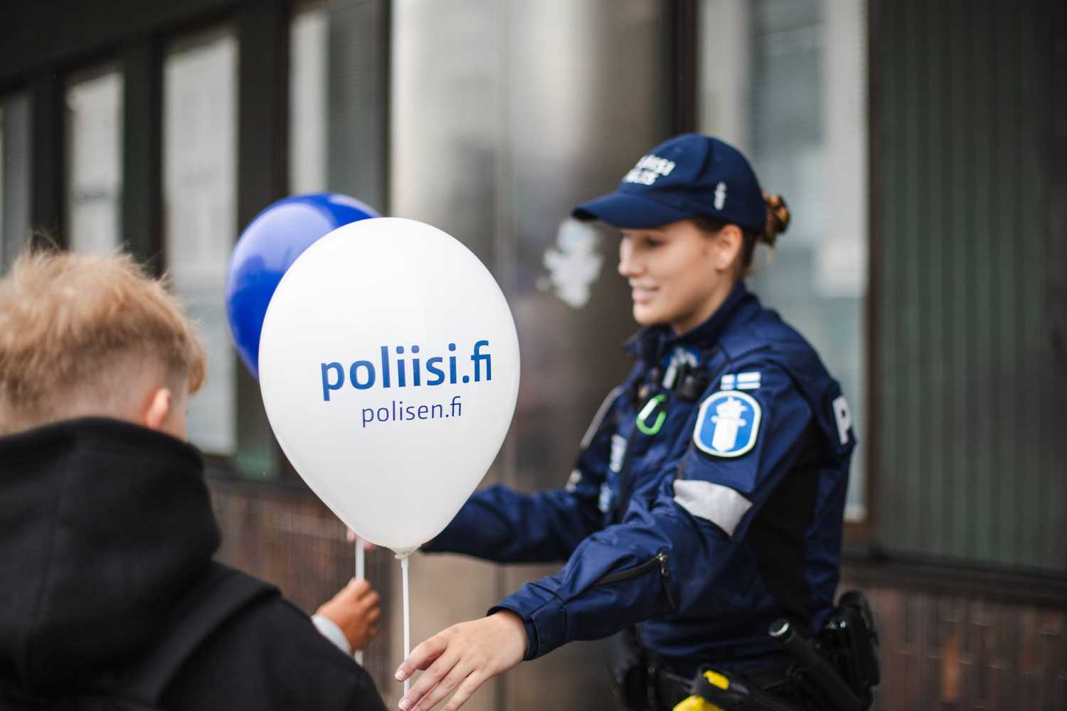 En poliskvinna i uniform delar ut ballonger till människor på Polisens dag. Texten på ballongerna är poliisi.fi, polisen.fi.