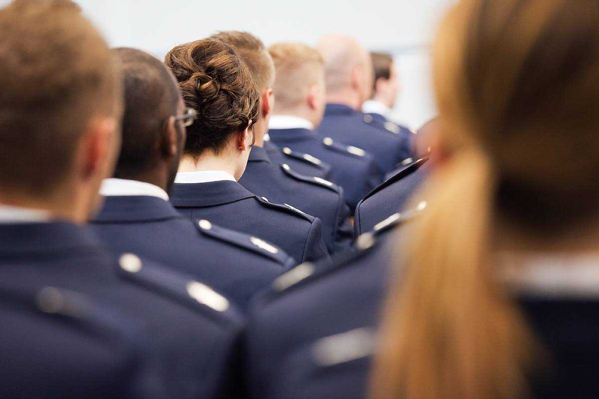 Rows of police officers in formal police clothing taking an ethical oath at a swearing-in ceremony with their backs to the camera and their shoulders in line. 