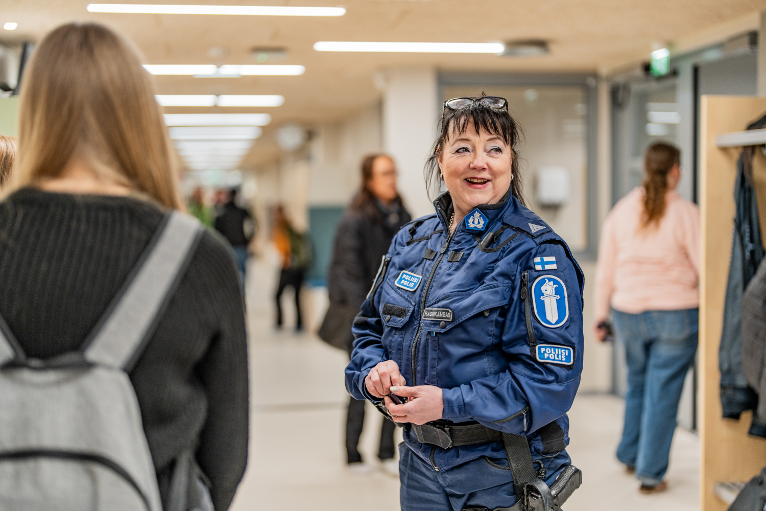 A police officer is standing in a school corridor and smiling.