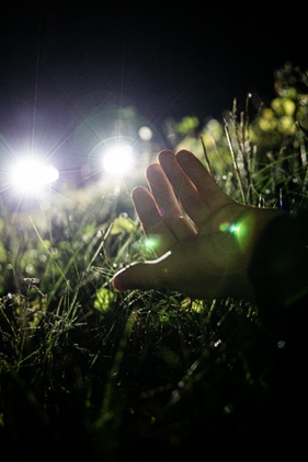 Onnettomuudessa loukkaantuneen käsi nurmella, jonka valaisee taustalla olevan ajoneuvon valot.