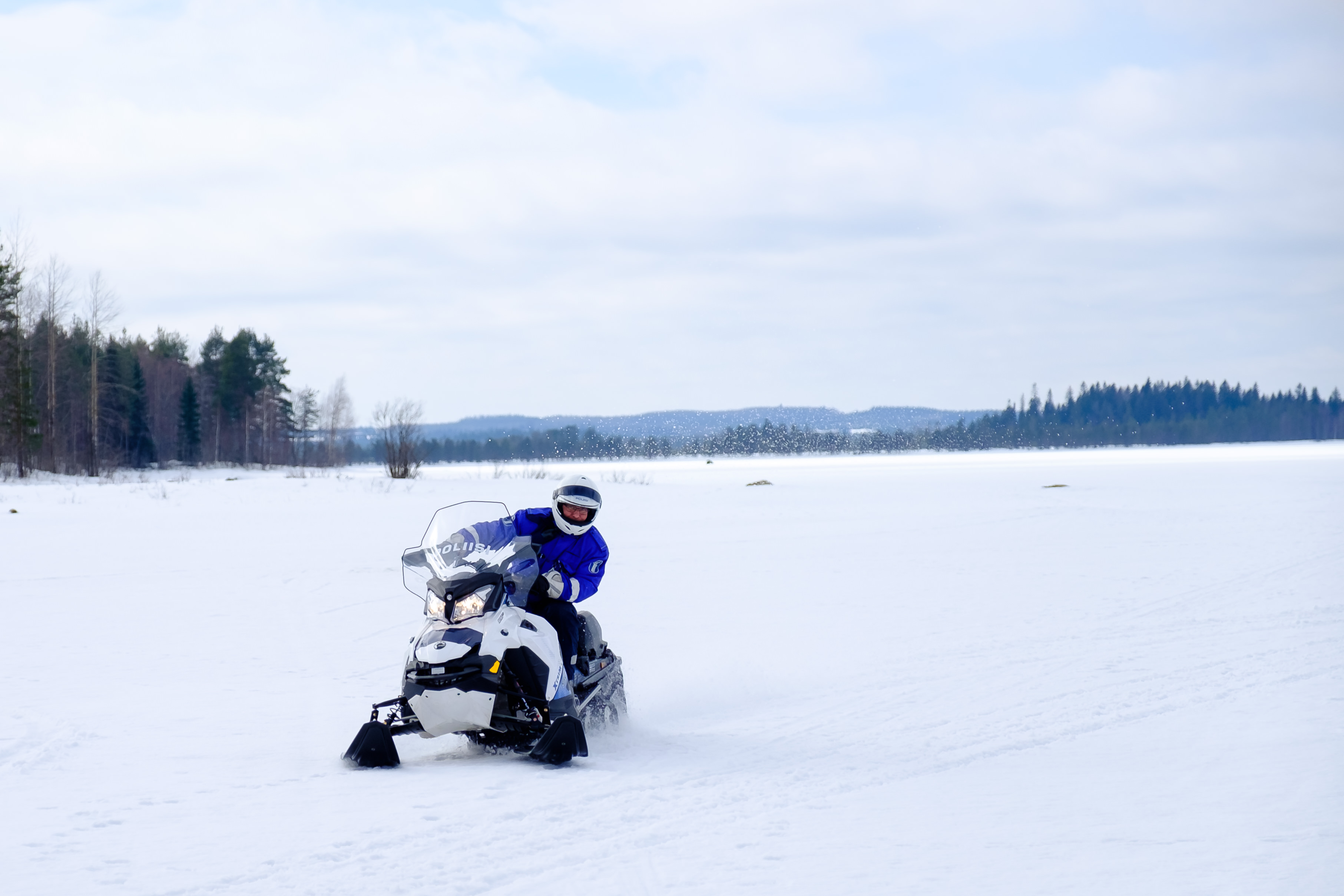 A police officer is riding a snowmobile on snowy terrain, possibly on the ice of a lake.