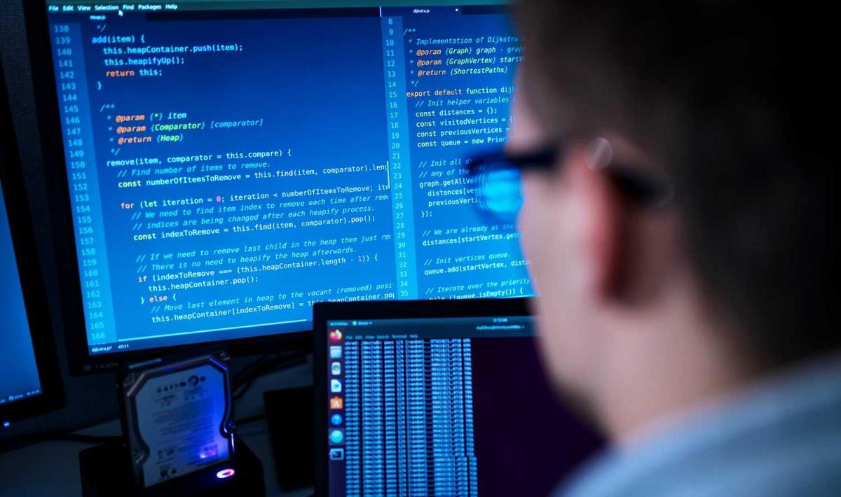 Tietokoneen ruutu, jossa koodikieltä. Oikealla sivuprofiili silmälasipäisestä miehestä.