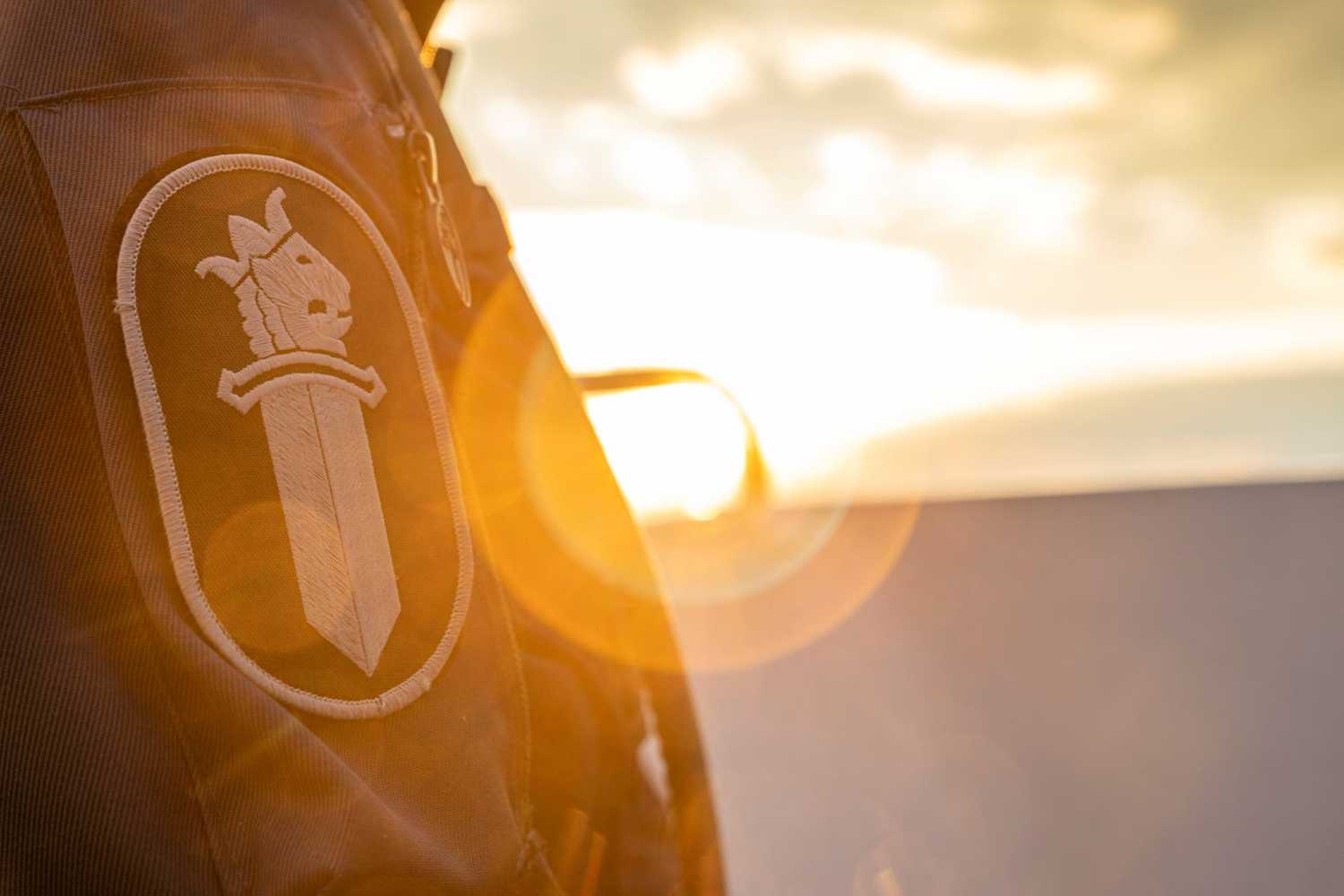 Poliisin miekkaleijona takin hihassa, taustalla auringonlasku.