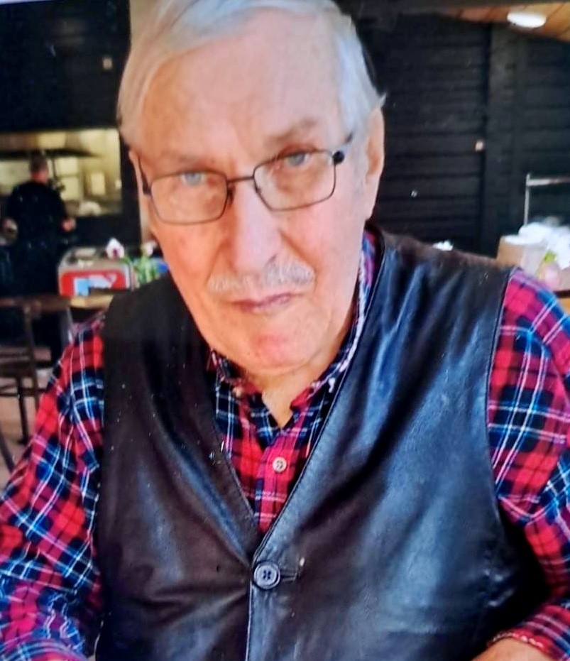 Rintakuva 86- vuotiaasta vaaleahiuksisesta miehestä. Päällään sinipunaraidallinen kauluspaita ja musta nahkaliivi. Silmälasit.