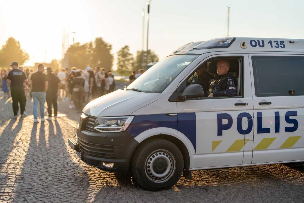 Poliserna sitter i en polisbil och i bakgrunden syns ungdomar.