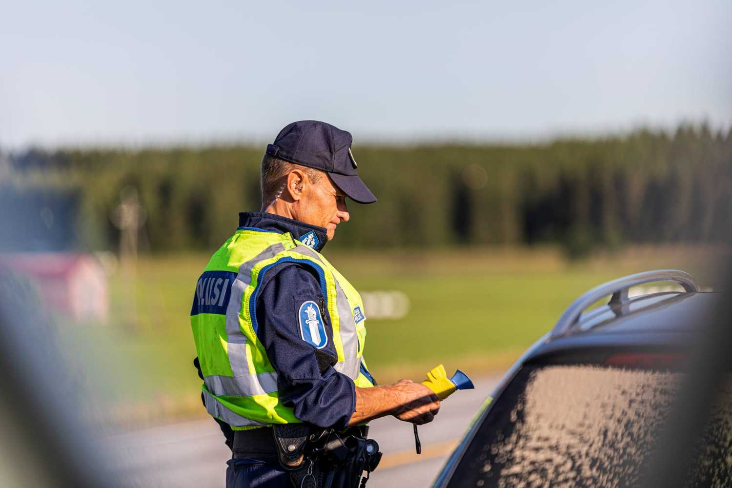 Virkapukuinen poliisimies seisoo auton vieressä kädessään alkometri.