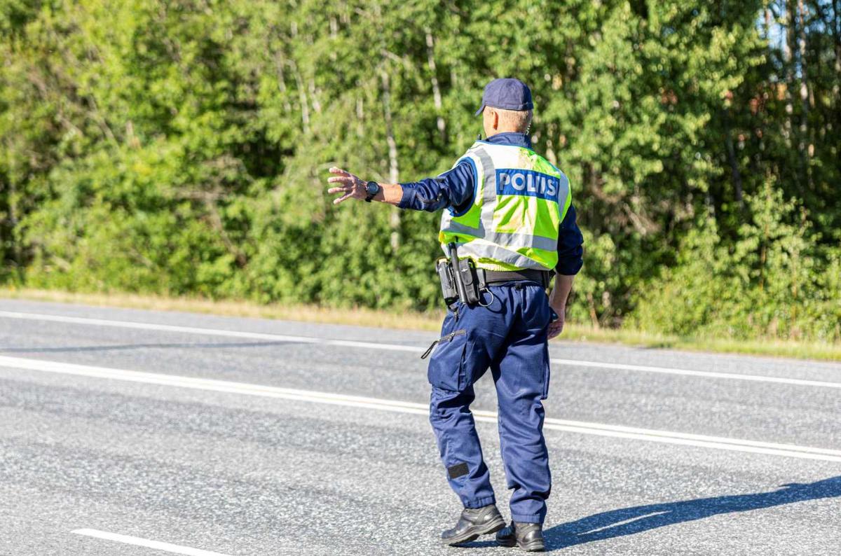 A policeman wearing a reflective vest directs traffic to the side of the road.