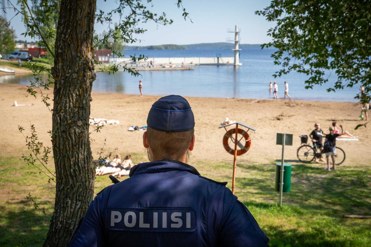 A sandy beach with people. The police are watching the situation from a distance.