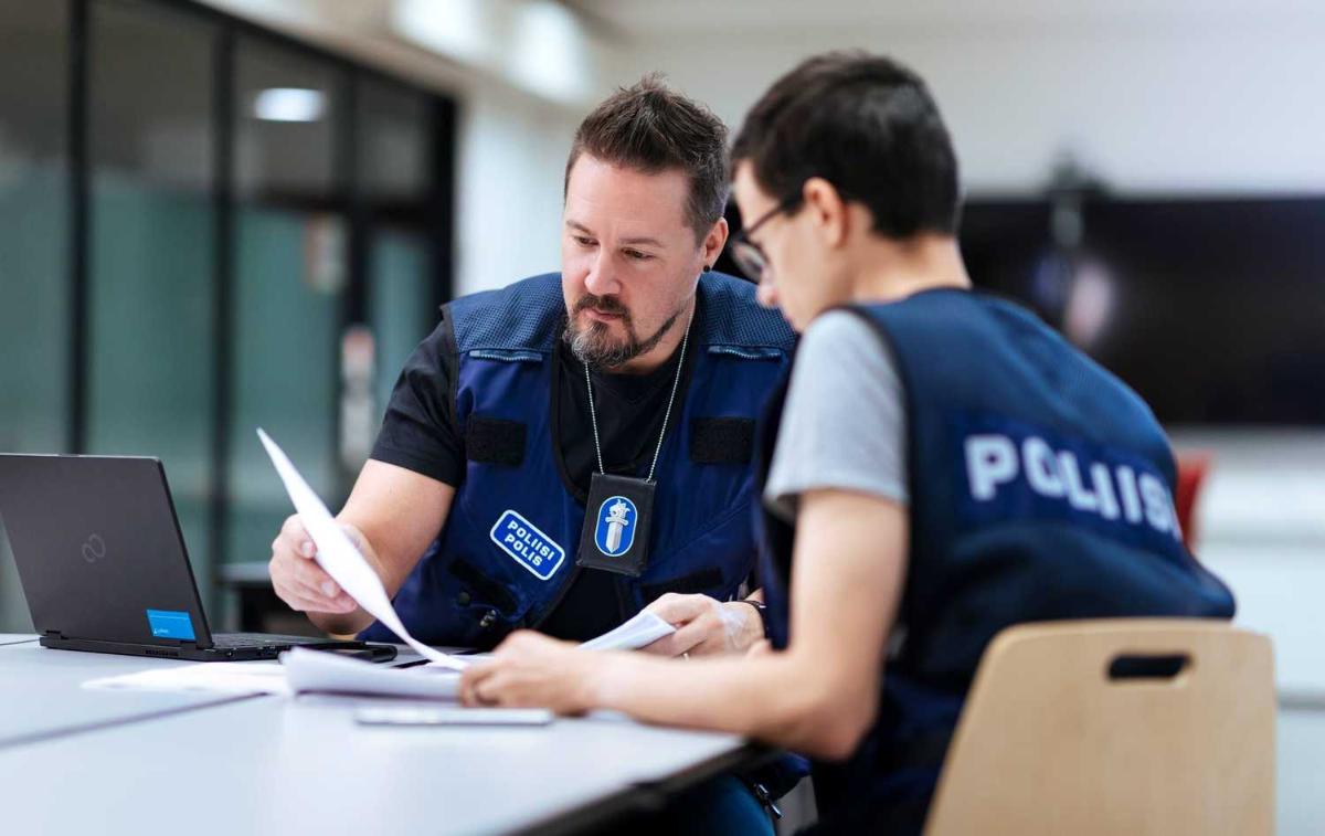 Kaksi poliisimiestä istuu pöydän ääressä paperita katsellen.