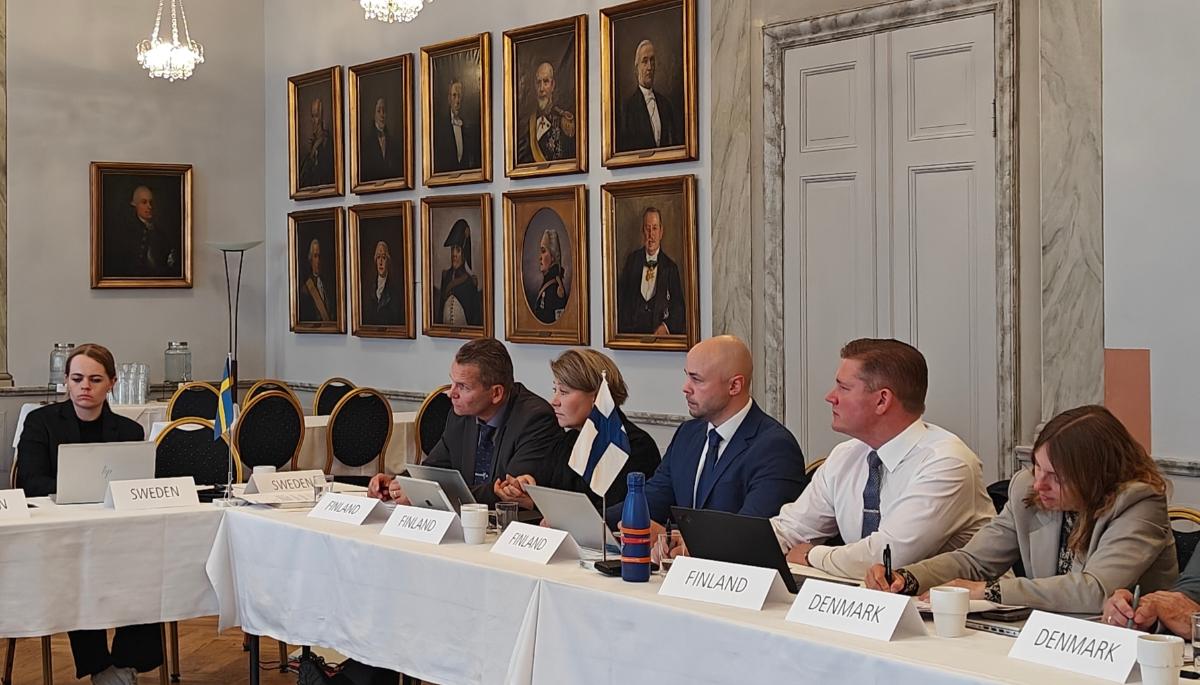 Kuusi henkilöä istuu pitkän pöydän ääressä.