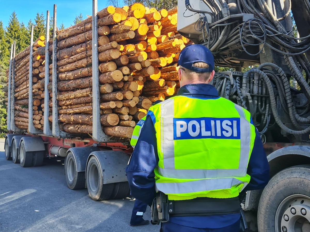 A policeman wearing a high-visibility vest checks a truck loaded with logs.